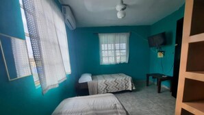 A room with two beds, a ceiling fan, a window with curtains, a TV mounted on the wall, and a wooden shelf. - Casa Fovissste 1 (Linares)