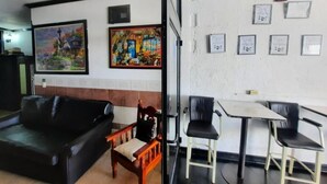 Une pièce comprenant un canapé en cuir noir, une chaise en bois, une petite table et une chaise noire. Deux tableaux ornent le mur, ainsi que plusieurs certificats ou affiches encadrés.