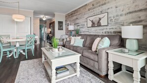 Ein Wohnzimmer mit Holzwand, einem grauen Sofa, einem weißen Couchtisch und einem weißen Beistelltisch.