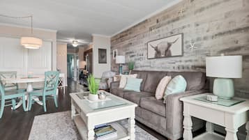 A living room with a wooden wall, a grey sofa, a white coffee table, and a white side table.