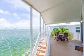 A covered balcony with a table and chairs, overlooking a body of water and a distant island. - Oceanfront, Heated Pool, Boat Dock, Upscale #214 (Cudjoe Key)