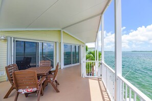 A covered outdoor area with a table and chairs, a railing, and a view of the ocean. - Oceanfront, Heated Pool, Boat Dock, Upscale #214 (Cudjoe Key)