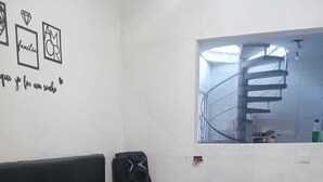 Une salle d’attente équipée d’un banc, d’une petite table, d’un haut-parleur et d’une fenêtre donnant sur un escalier.
