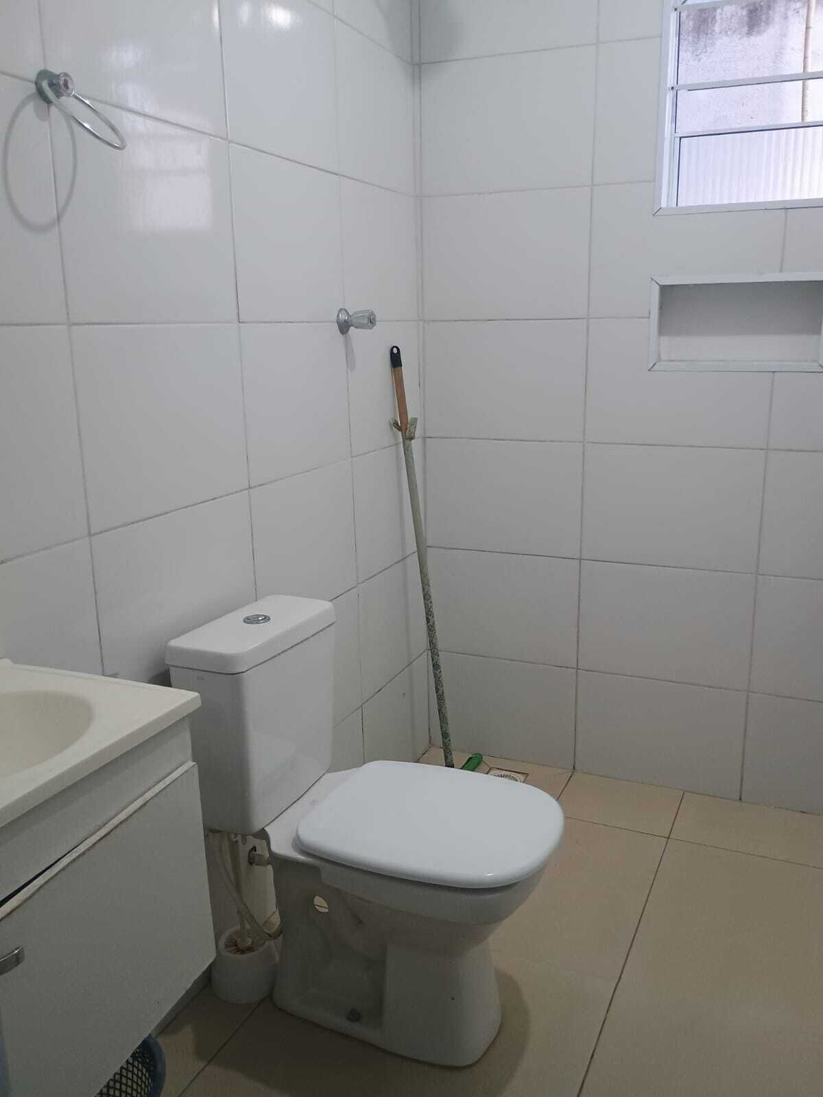 A bathroom with a toilet, sink, and a mop leaning against the wall.