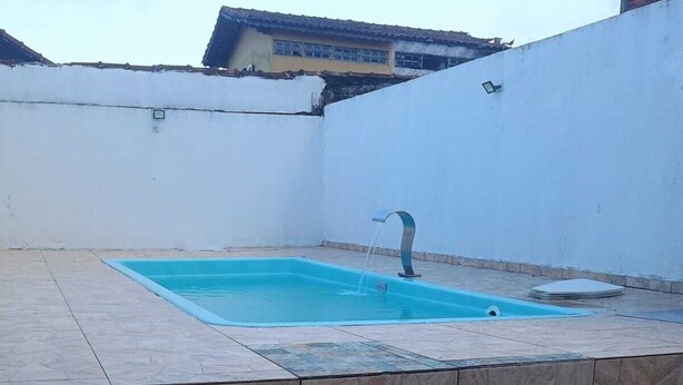 Une piscine avec une fontaine, entourée d’un mur blanc et dotée d’un sol carrelé.