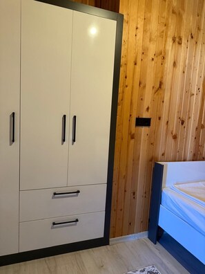 Quarto com cama, parede de painéis de madeira e guarda-roupa com gavetas e portas.