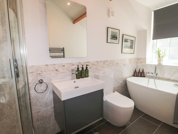 Ein modernes Badezimmer mit Duschkabine aus Glas, einem weißen Waschbecken mit grünen Seifenspendern, einer weißen Toilette und einer weißen Badewanne.