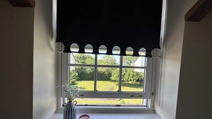 Una finestra con davanzale bianco, una tenda avvolgibile nera, un vaso con fiori e una ciotola rosa.