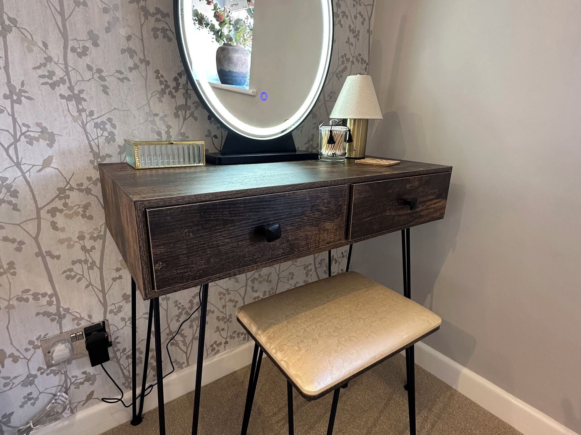 A vanity with a mirror, a lamp, and a bench.