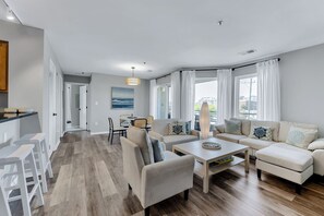 A modern living room with a sofa set, a coffee table, and a dining area with chairs. - Virginia Beach Condo With Balcony & Pool (Virginia Beach)