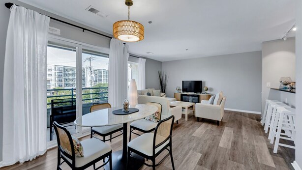 A modern living room with a dining area, a TV, and a balcony with curtains. - Virginia Beach Condo With Balcony & Pool (Virginia Beach)