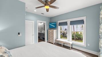Un dormitorio con cama, ventilador de techo, ventana con vistas, cómoda y un banco.