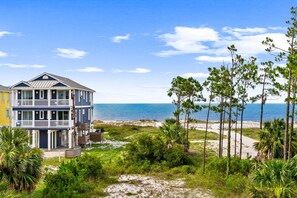 A beachfront property with a large two-story house, a balcony, and a view of the ocean.