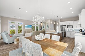 A modern kitchen with white cabinetry, stainless steel appliances, and a dining area with wicker chairs and a wooden table.