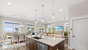 Una cocina moderna con una isla grande, iluminación colgante y vista al océano.