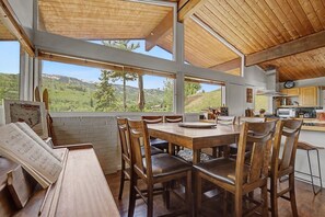 A dining area with a wooden table and chairs, a view of the outdoors, and a kitchen area with wooden cabinets. - Classic Snowmass Village Ski Chalet,  Ski-in! (Snowmass Village)