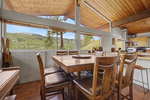 A dining area with a wooden table and chairs, a view of the outdoors, and a kitchen area with wooden cabinets. - Classic Snowmass Village Ski Chalet,  Ski-in! (Snowmass Village)