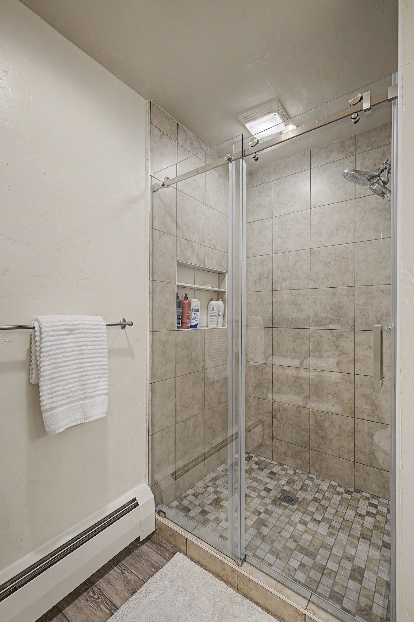 A shower with a glass door, a white towel on a rack, and toiletries on a shelf.