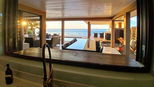 A modern interior with a large window overlooking the sea, a pool, and a dining area.