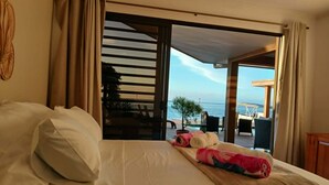 A hotel room with a bed, a view of the sea, and a balcony with outdoor furniture.