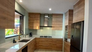 A modern kitchen with wooden cabinets, a stainless steel refrigerator, and a large island with a sink.