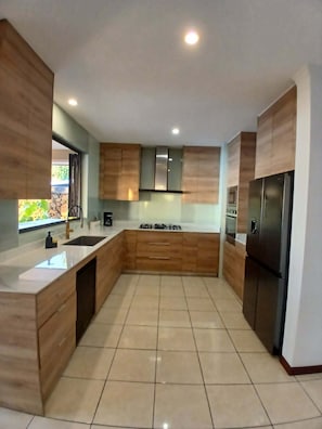 Eine moderne Küche mit Holzausstattung, einem Edelstahlkühlschrank und einer großen Kochinsel mit Spüle.