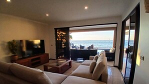 A living room with a TV, sofa, and a view of the sea.