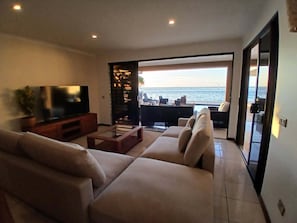 Ein Wohnzimmer mit Fernseher, Sofa und Meerblick.