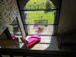 Una habitación con un ventanal amplio, una silla rosa y vistas a un jardín.