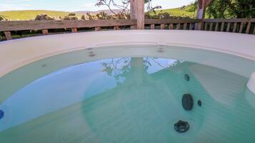 A hot tub with a wooden deck and a view of a grassy landscape.
