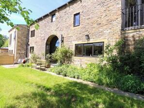 A stone building with a large arched doorway, a wooden bench, and a small garden area. - Bib Knowl Farm (Rochdale)