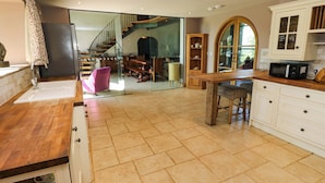 Cozinha com bancada de madeira, armários brancos e piso ladrilhado.