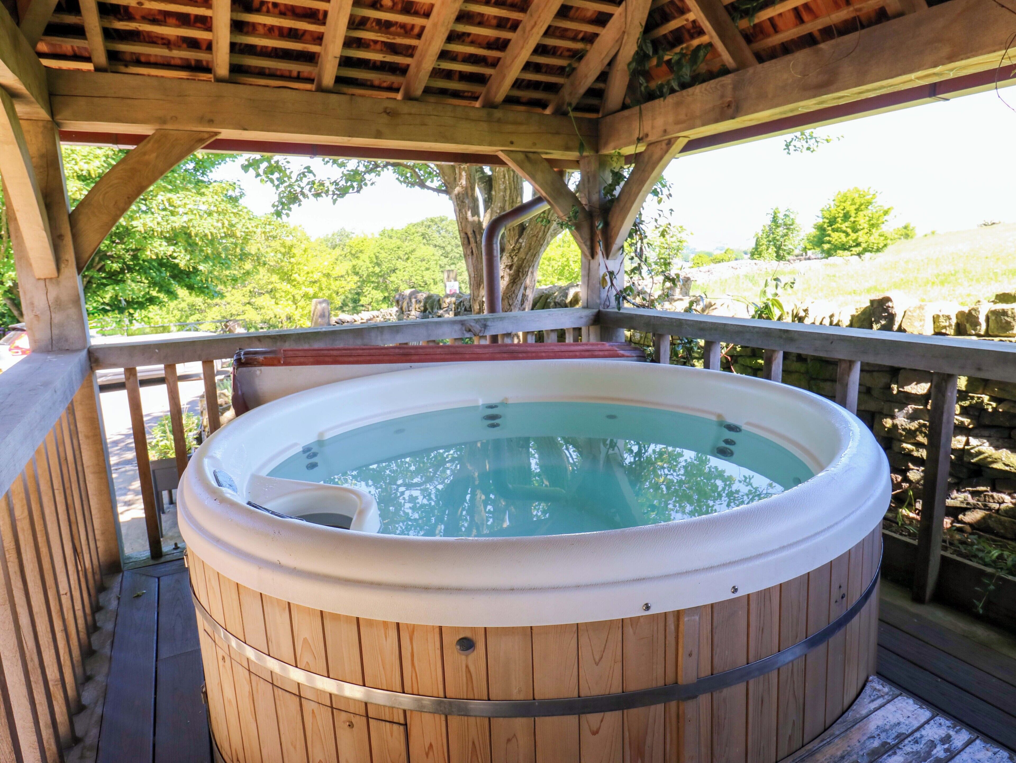 A wooden hot tub on a wooden deck with a pergola overhead.