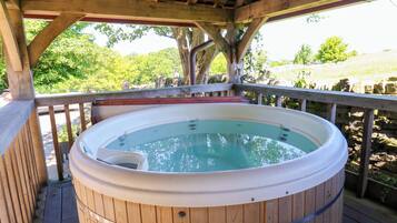 A wooden hot tub on a wooden deck with a pergola overhead.
