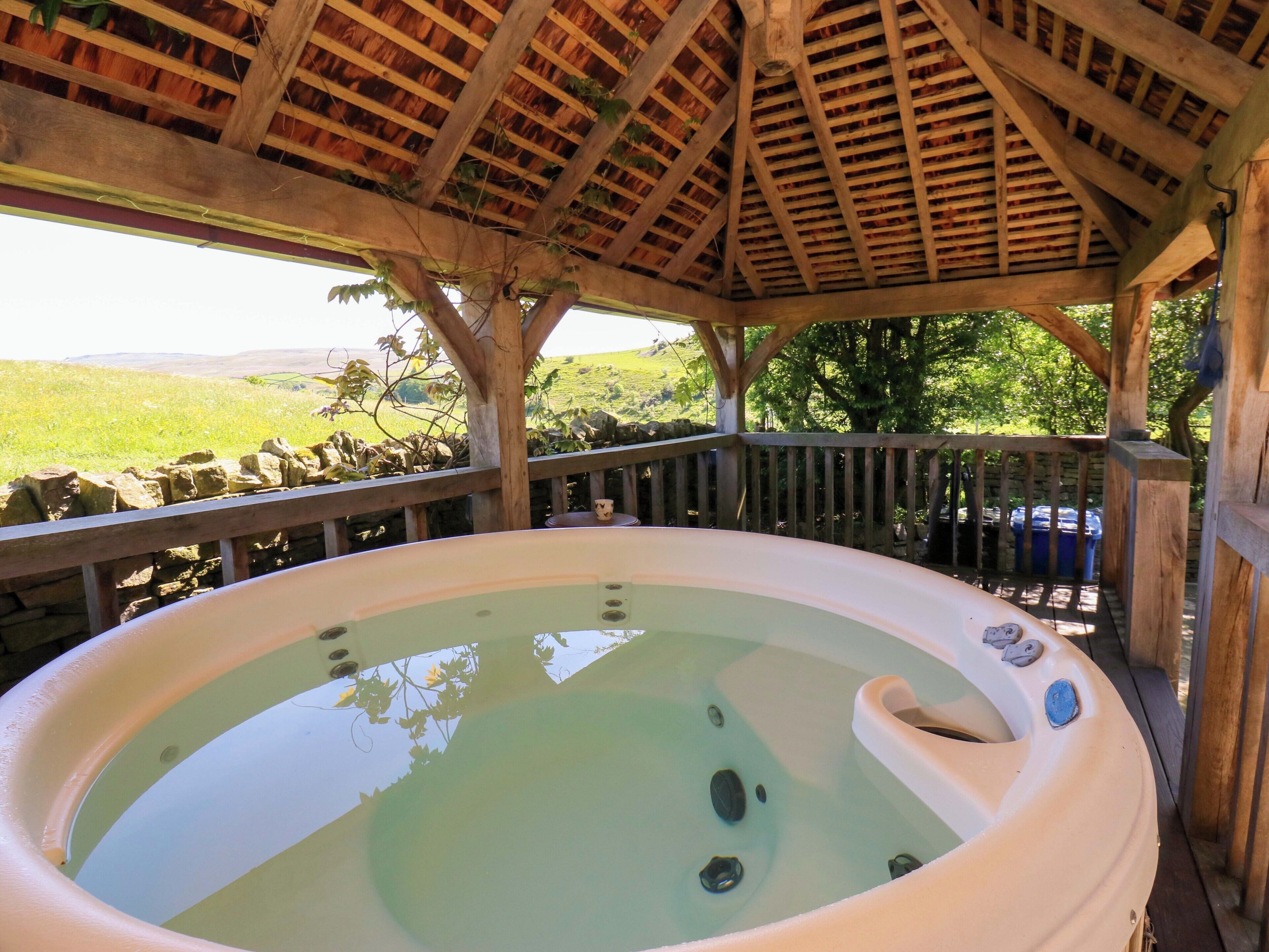 A hot tub under a wooden gazebo with a stone wall and a view of the countryside.