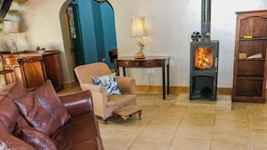 Uma sala de estar com um sofá de couro, uma poltrona estampada, uma mesinha com abajur, lareira e um armário de madeira.