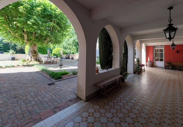A covered outdoor area with a tiled floor, benches, and a tree.