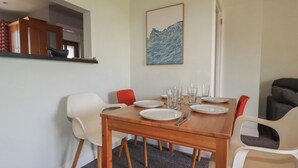 A dining area with a wooden table set for four, surrounded by white and red chairs. - Carnweather (Newquay)