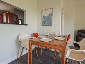 A dining area with a wooden table set for four, surrounded by white and red chairs. - Carnweather (Newquay)