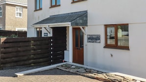 A two-story residential building with a white exterior, a dark roof, and a wooden door. - Carnweather (Newquay)