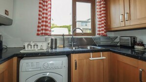 Uma cozinha compacta com armários de madeira, máquina de lavar, pia e janela com cortinas xadrez.
