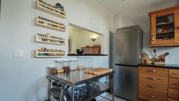 A kitchen with a stainless steel refrigerator, wooden cabinets, and a metal cart with kitchen utensils. - Carnweather (Newquay)