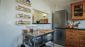 Uma cozinha com geladeira de aço inoxidável, armários de madeira e um carrinho de metal com utensílios de cozinha.