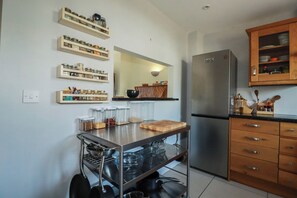 A kitchen with a stainless steel refrigerator, wooden cabinets, and a metal cart with kitchen utensils. - Carnweather (Newquay)