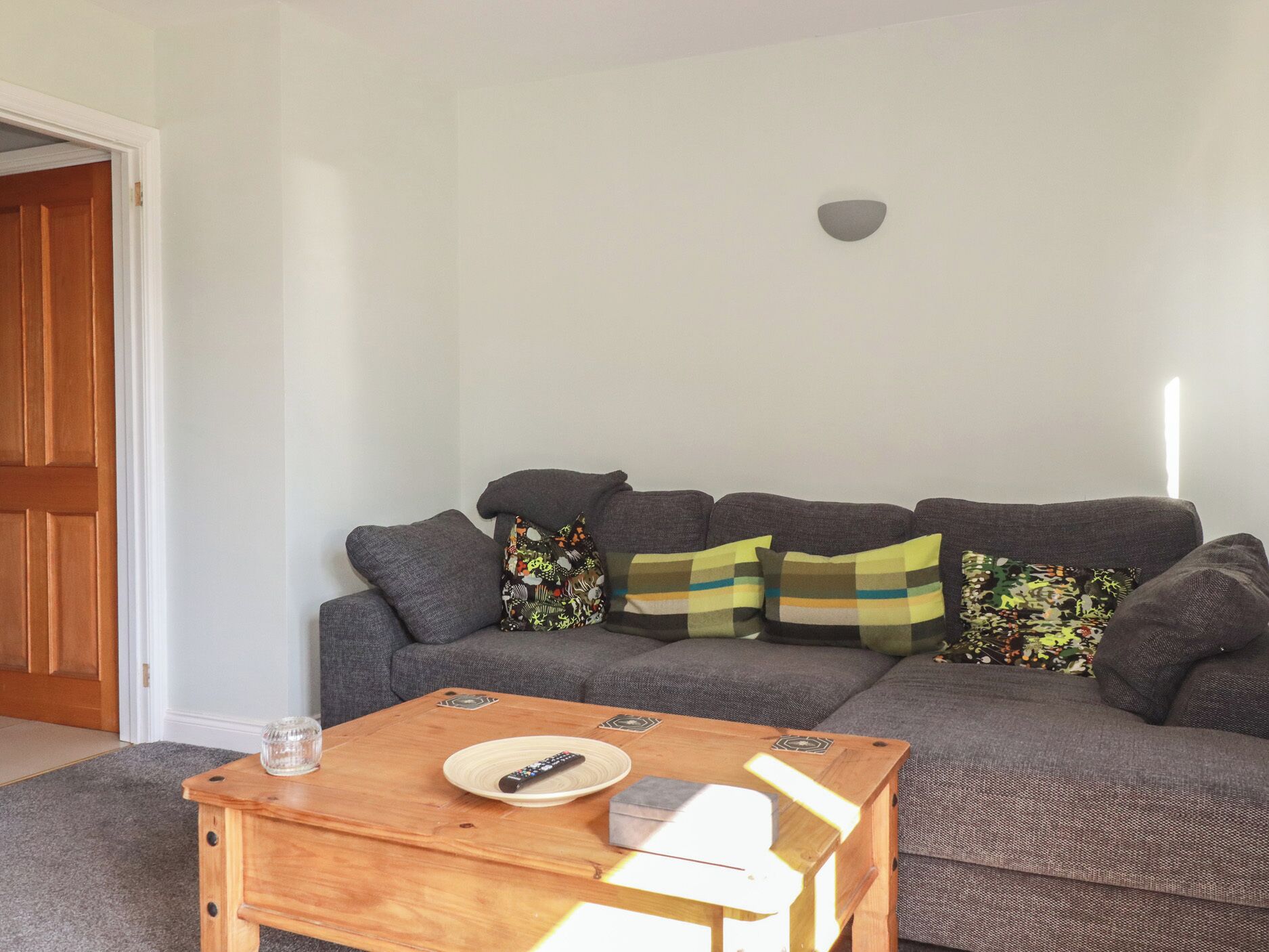Uma sala de estar com um sofá cinza, uma mesa de centro de madeira e um controle remoto sobre a mesa.