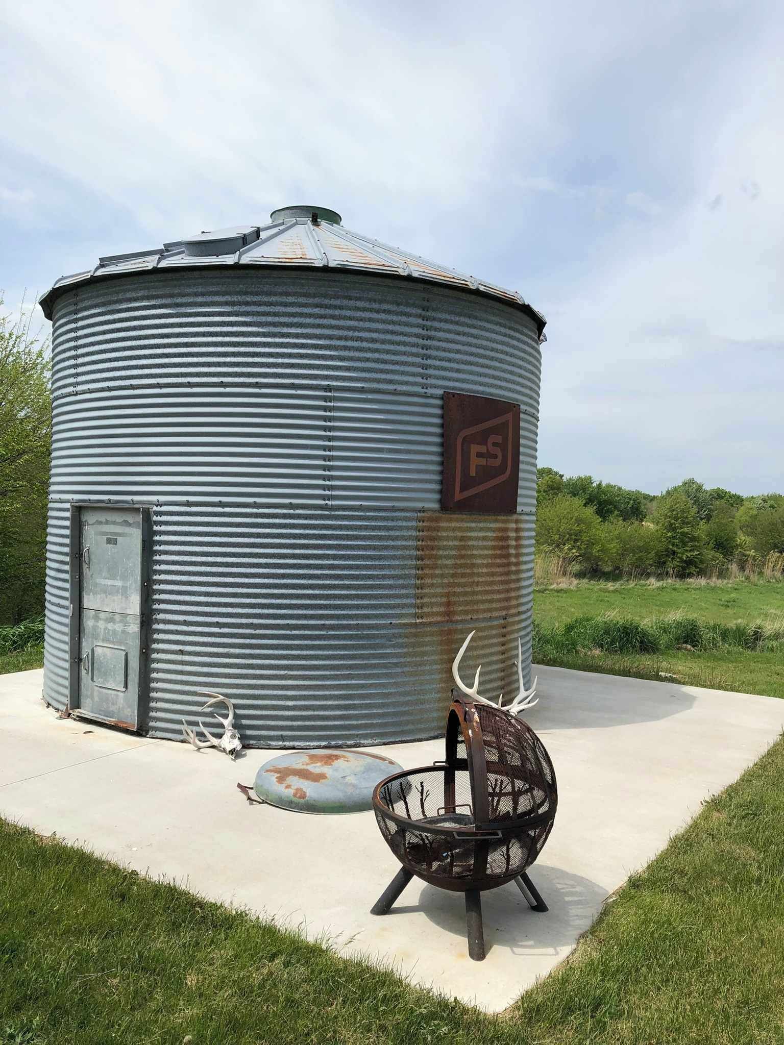 A cylindrical metal structure with a door and a logo, a metal chair, and antlers on the ground.