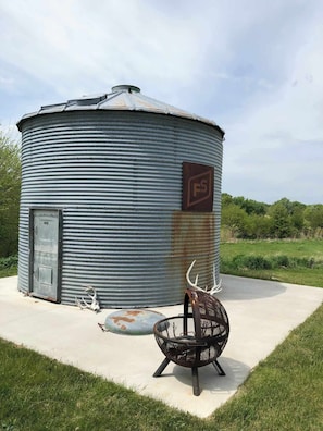 A cylindrical metal structure with a door and a logo, a metal chair, and antlers on the ground.