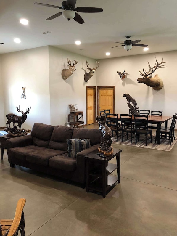 A living room with a brown sofa, a coffee table, a dining table with chairs, and mounted deer heads on the wall.