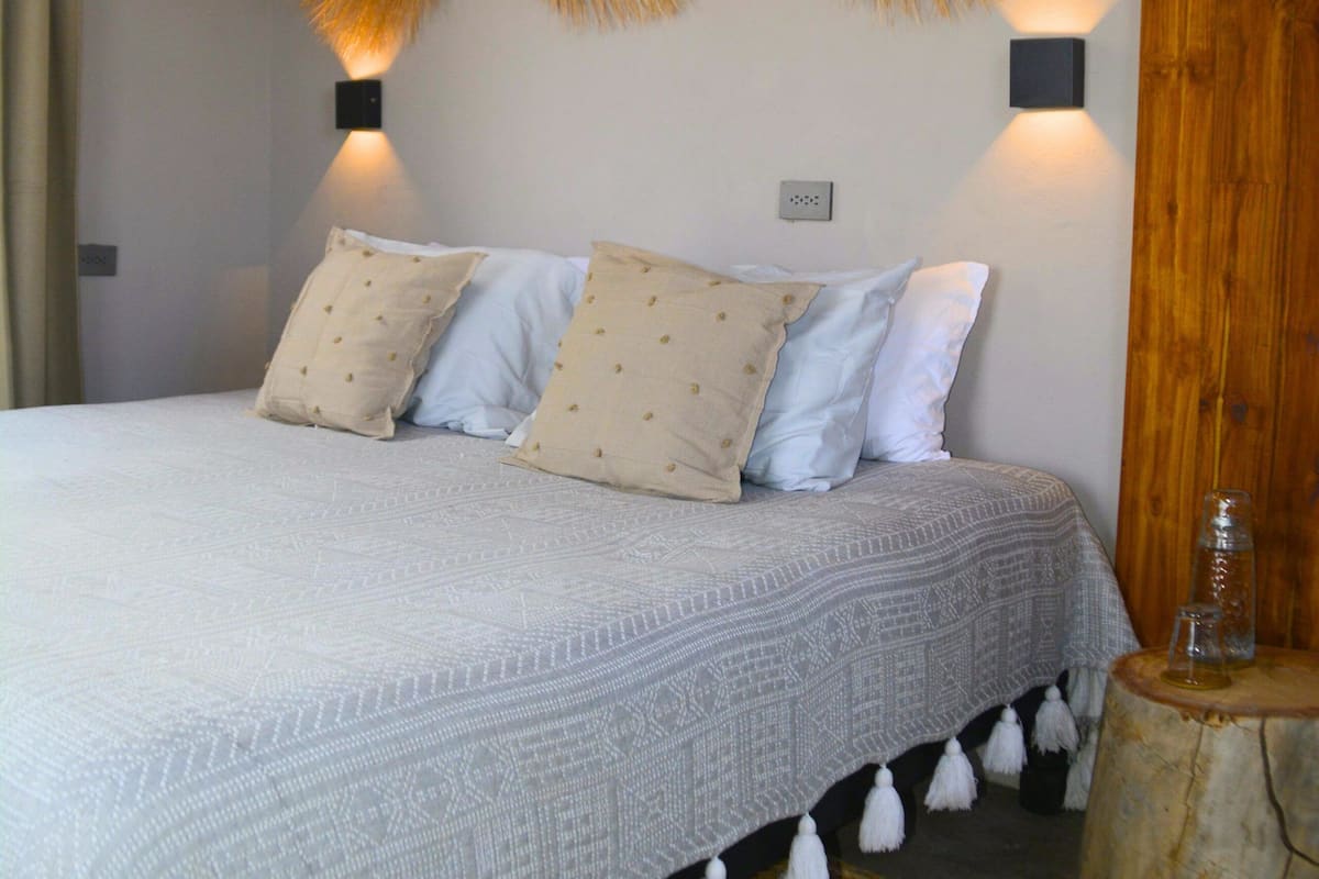 Una cama con una colcha estampada, dos lámparas de pared y un adorno trenzado en la pared.