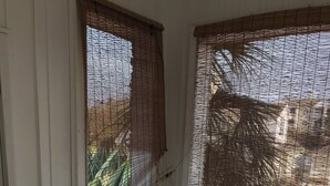 Ein Zimmer mit einem einzelnen weißen Stuhl, einem Fenster mit Bambusrollos und Blick auf ein geparktes Auto.